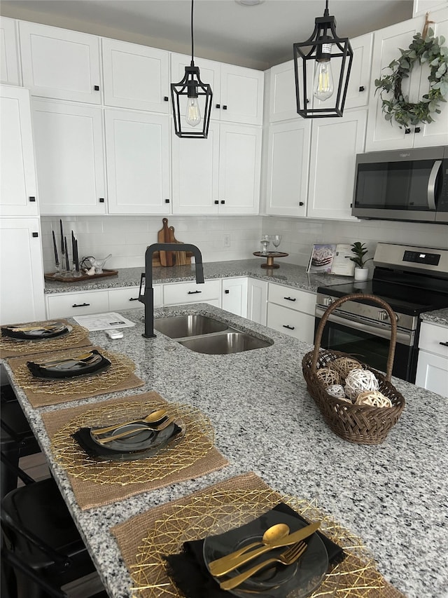 kitchen featuring tasteful backsplash, sink, white cabinets, stainless steel appliances, and decorative light fixtures