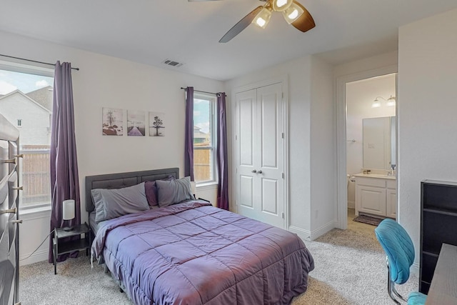 bedroom with connected bathroom, ceiling fan, multiple windows, light carpet, and a closet