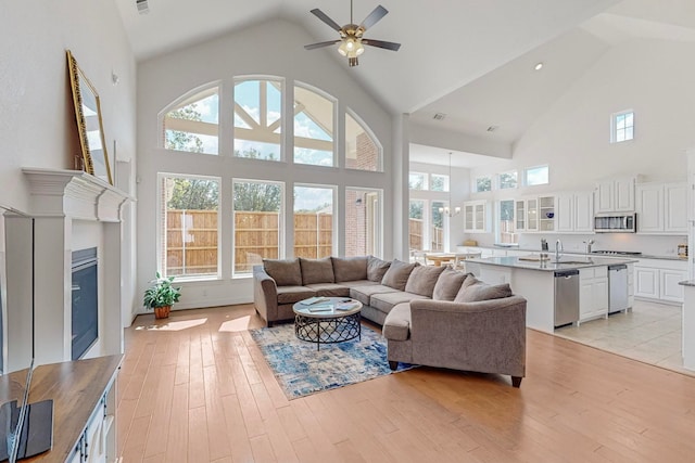 living room with ceiling fan, light hardwood / wood-style floors, sink, and high vaulted ceiling