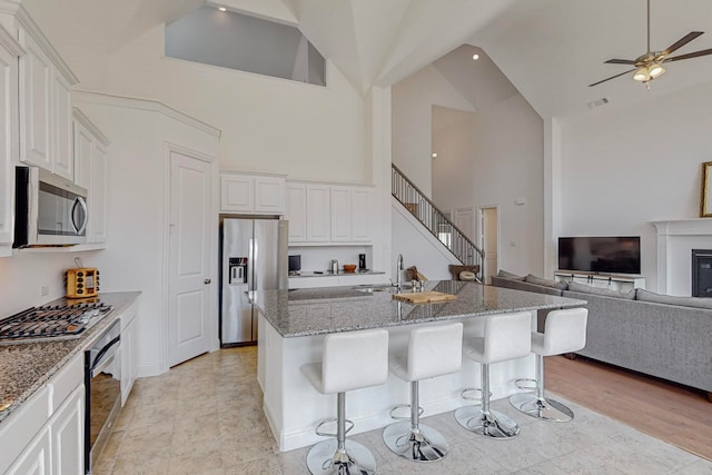 kitchen featuring white cabinetry, stainless steel appliances, light stone counters, a breakfast bar area, and a kitchen island with sink