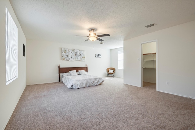 carpeted bedroom with a walk in closet, ceiling fan, a closet, and a textured ceiling