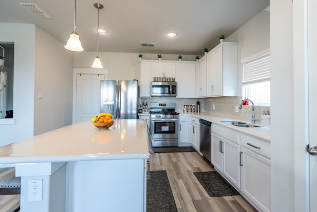 kitchen featuring white cabinets, pendant lighting, sink, stainless steel appliances, and light wood-type flooring