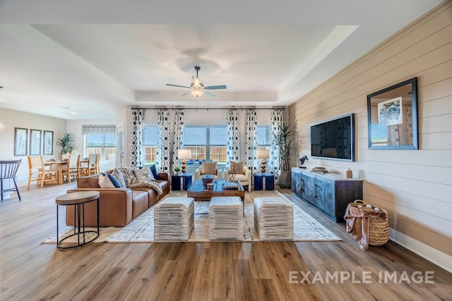 living room with hardwood / wood-style floors, ceiling fan, a wealth of natural light, and wood walls