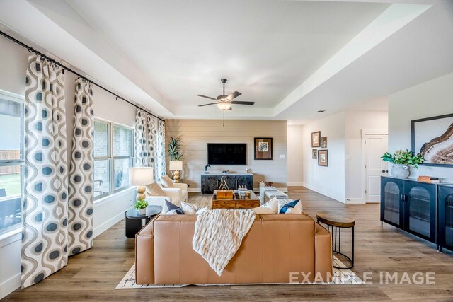 living room with a tray ceiling, ceiling fan, and light wood-type flooring