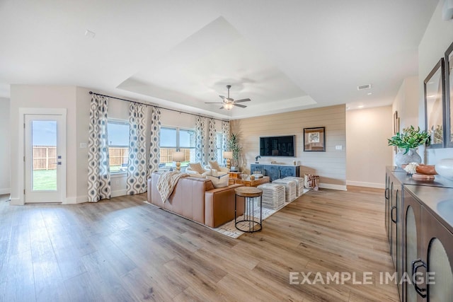 living room featuring a raised ceiling, ceiling fan, and light wood-type flooring