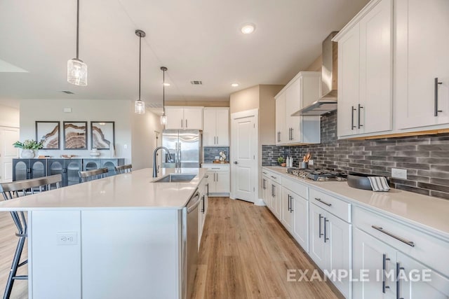 kitchen with a breakfast bar, wall chimney range hood, a kitchen island with sink, and appliances with stainless steel finishes