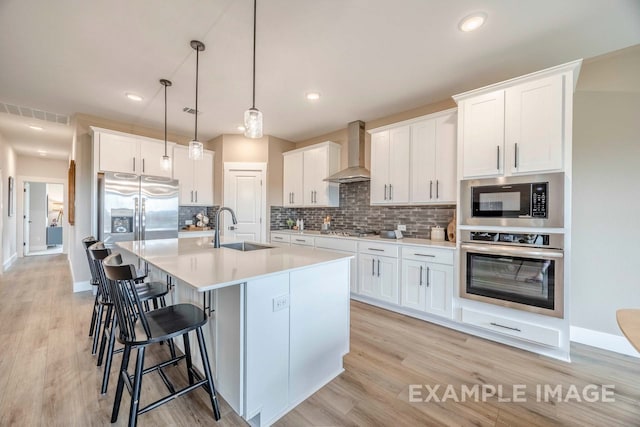 kitchen with sink, hanging light fixtures, wall chimney exhaust hood, appliances with stainless steel finishes, and white cabinetry