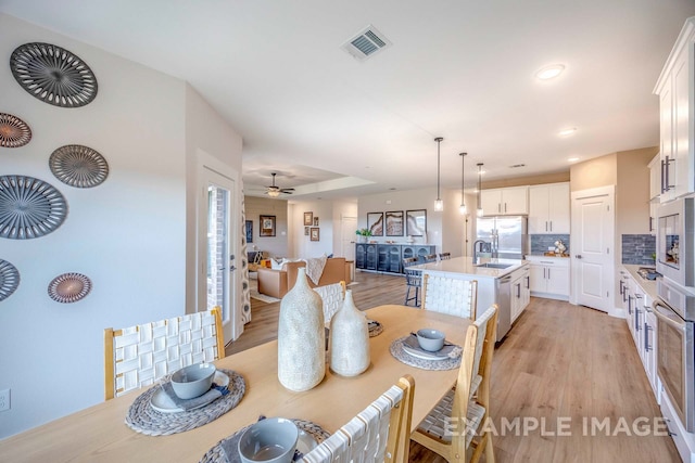 dining area with ceiling fan, sink, and light hardwood / wood-style flooring