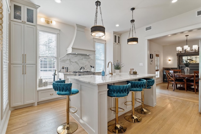 kitchen featuring light wood-type flooring, a center island with sink, and decorative light fixtures