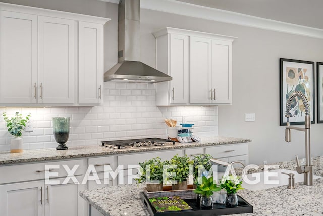 kitchen with decorative backsplash, white cabinetry, stainless steel gas stovetop, and wall chimney exhaust hood