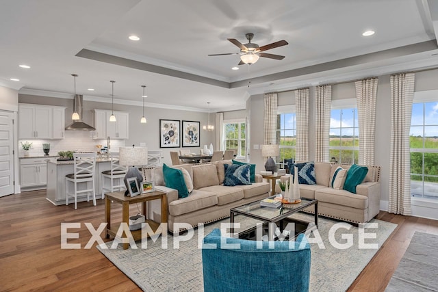 living room featuring ceiling fan with notable chandelier, light wood-type flooring, ornamental molding, and a tray ceiling