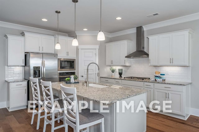 kitchen with white cabinetry, wall chimney exhaust hood, a center island with sink, and appliances with stainless steel finishes