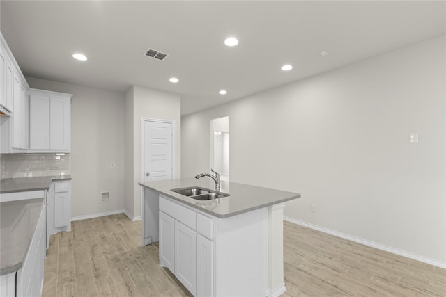 kitchen with a center island with sink, decorative backsplash, white cabinets, light hardwood / wood-style flooring, and sink