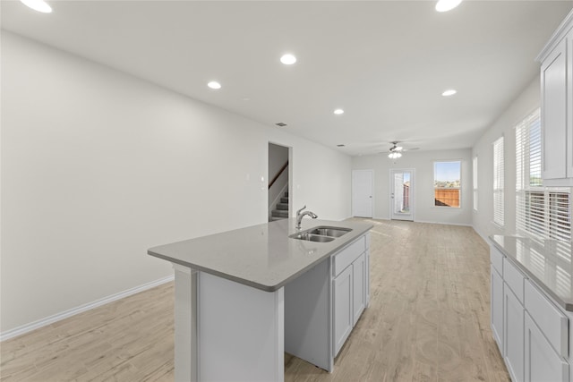 kitchen featuring white cabinets, light hardwood / wood-style floors, sink, stone countertops, and a center island with sink