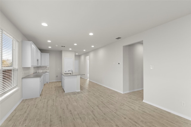 interior space featuring light hardwood / wood-style floors, decorative backsplash, a kitchen island with sink, white cabinets, and sink