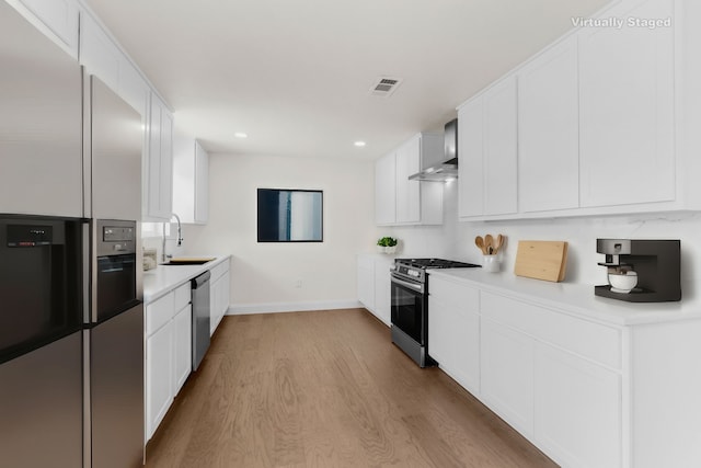 kitchen with sink, appliances with stainless steel finishes, wall chimney exhaust hood, light hardwood / wood-style flooring, and white cabinets