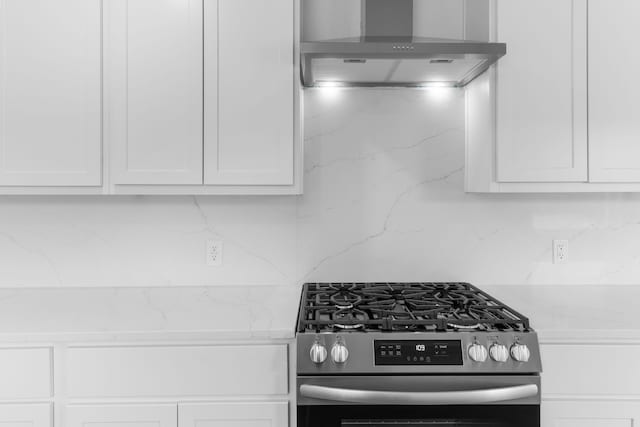 kitchen with light stone counters, gas stove, backsplash, white cabinets, and wall chimney range hood