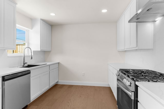 kitchen with white cabinetry, sink, appliances with stainless steel finishes, wall chimney range hood, and light wood-type flooring