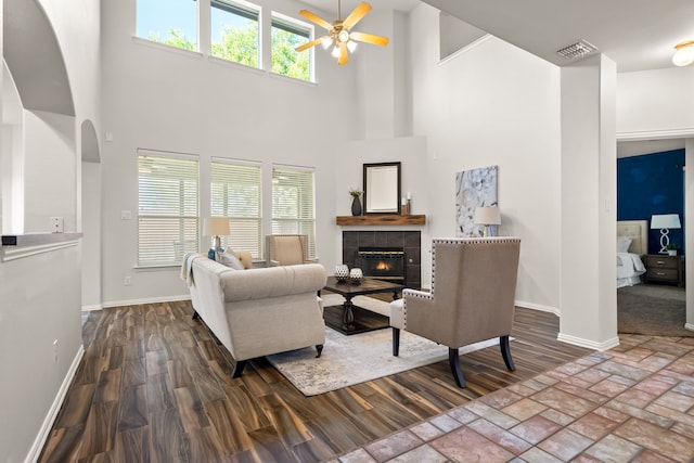 living room with ceiling fan, a tile fireplace, hardwood / wood-style floors, and a towering ceiling