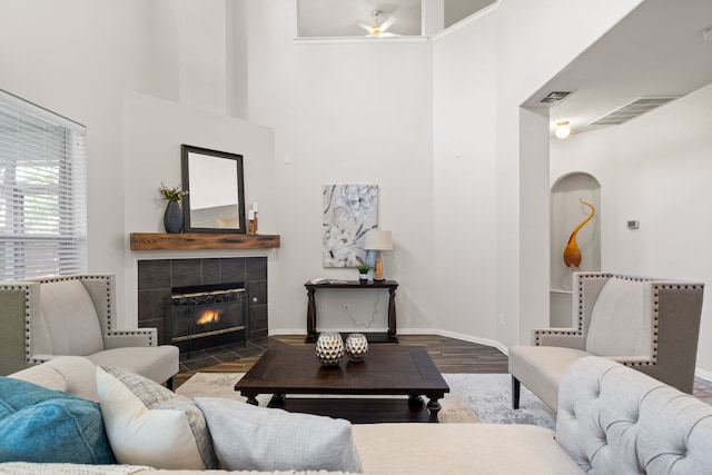 living room with a tiled fireplace, a towering ceiling, and dark hardwood / wood-style flooring