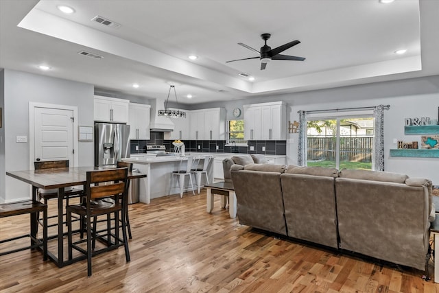 living room featuring light wood-type flooring, ceiling fan, and a tray ceiling