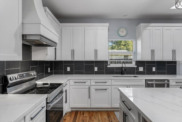 kitchen with white cabinets, appliances with stainless steel finishes, sink, light stone counters, and custom range hood