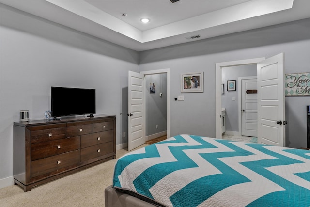 bedroom with light colored carpet, connected bathroom, and a tray ceiling