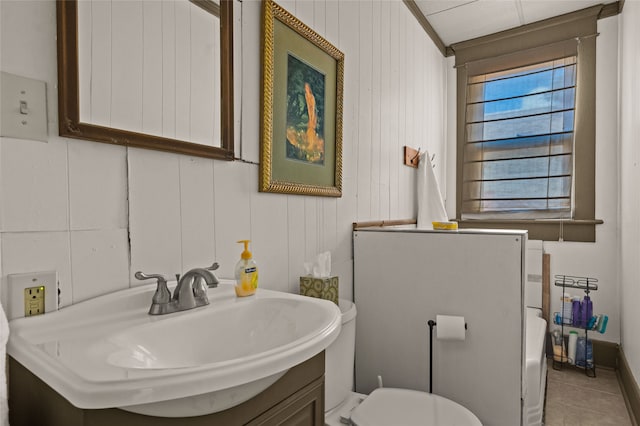 bathroom with toilet, tile patterned flooring, wood walls, and sink