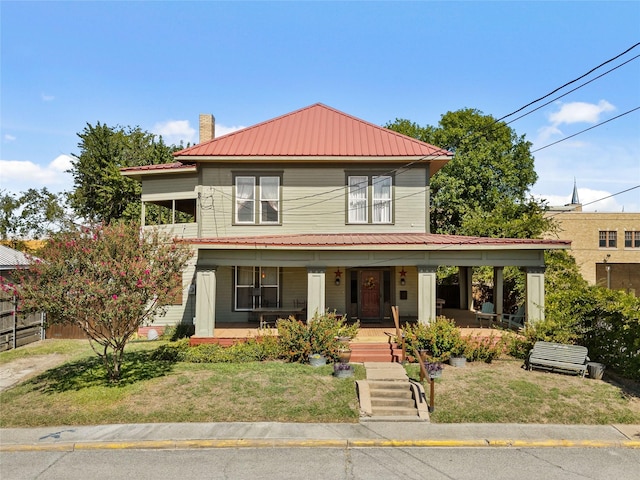 view of front of house with covered porch, a chimney, fence, a front lawn, and metal roof