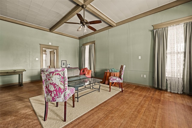 living area with a ceiling fan, a healthy amount of sunlight, beamed ceiling, and wood finished floors