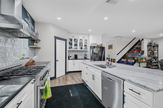 kitchen with wall chimney range hood, white cabinets, sink, light hardwood / wood-style floors, and stainless steel appliances