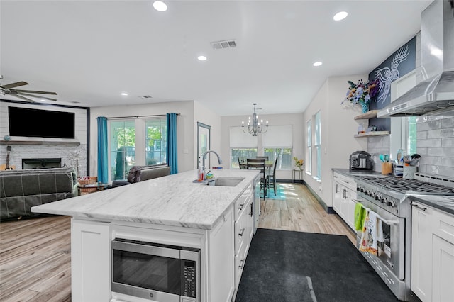 kitchen with wall chimney range hood, appliances with stainless steel finishes, sink, an island with sink, and white cabinetry