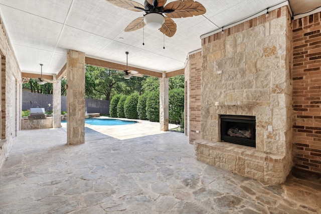 view of patio / terrace with a fenced in pool, ceiling fan, an outdoor kitchen, and an outdoor stone fireplace