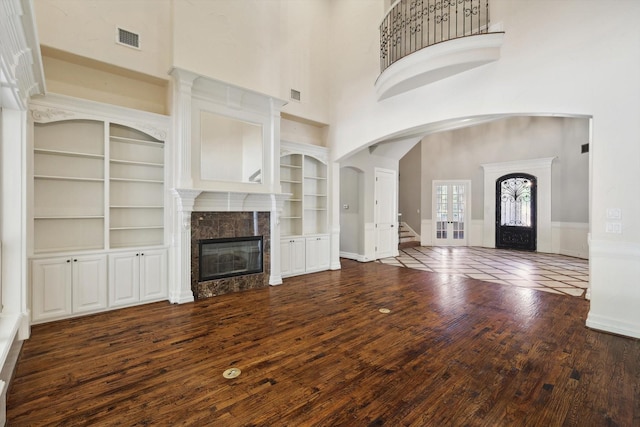 unfurnished living room featuring built in shelves, dark hardwood / wood-style floors, a towering ceiling, and a fireplace