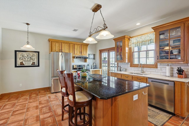 kitchen with appliances with stainless steel finishes, hanging light fixtures, backsplash, a kitchen island, and sink