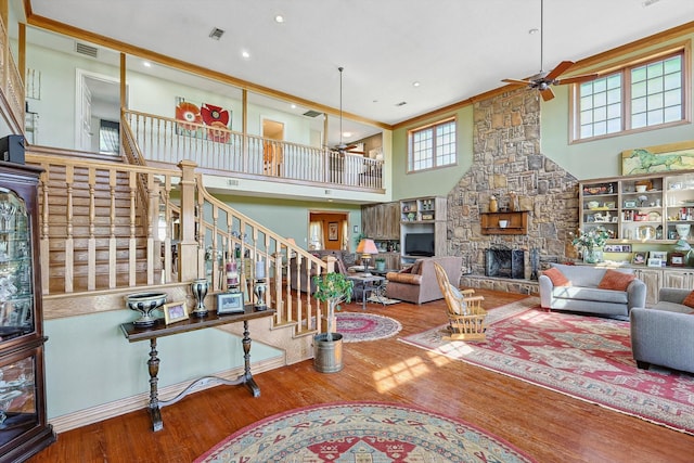 living room featuring a high ceiling, wood-type flooring, ceiling fan, and a stone fireplace