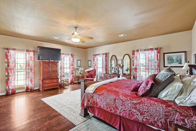 bedroom featuring multiple windows, dark hardwood / wood-style floors, ceiling fan, and a textured ceiling