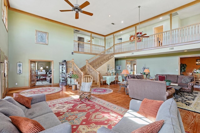 living room with ceiling fan, light wood-type flooring, a towering ceiling, and ornamental molding