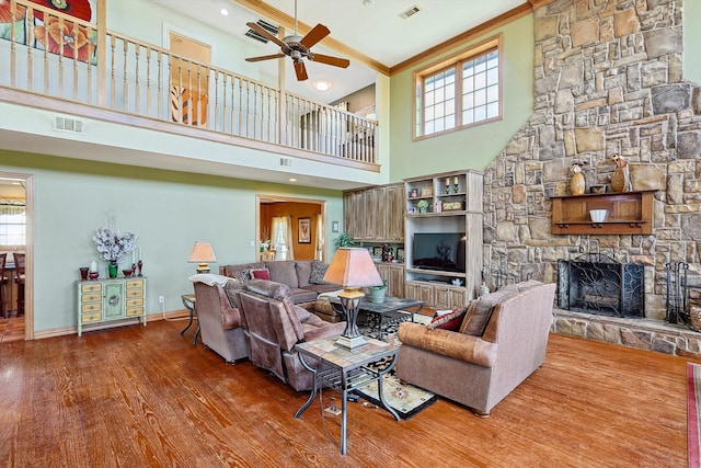 living room featuring a stone fireplace, wood-type flooring, a high ceiling, and a wealth of natural light