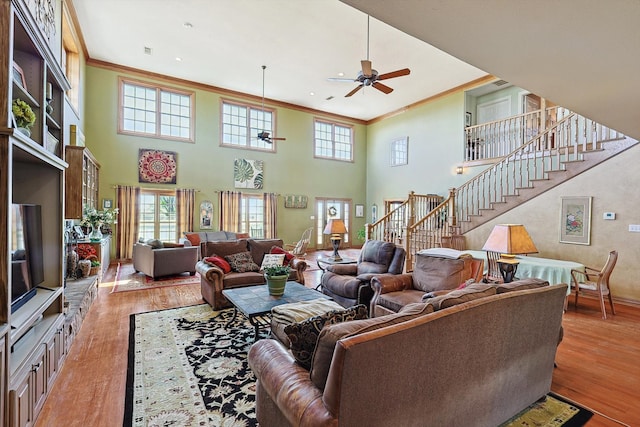 living room featuring crown molding, light hardwood / wood-style floors, a towering ceiling, and ceiling fan