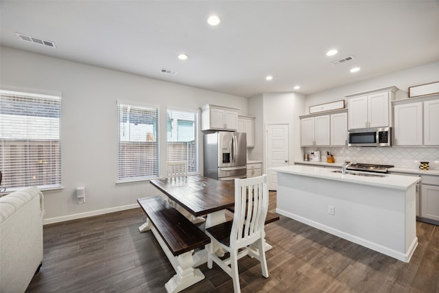 kitchen with a kitchen island with sink, appliances with stainless steel finishes, backsplash, and dark hardwood / wood-style flooring