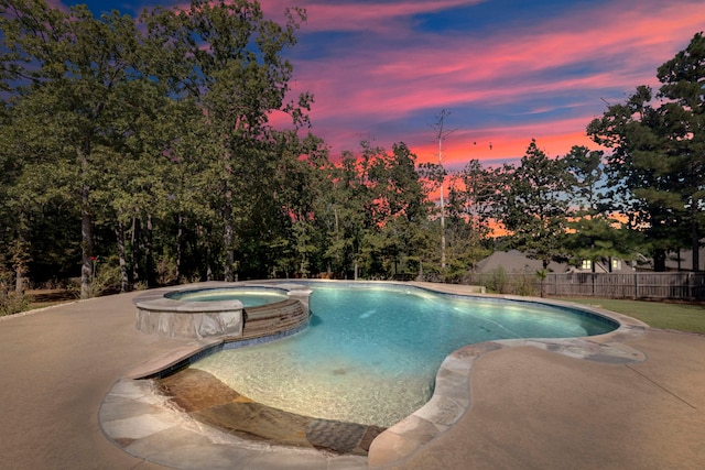 pool at dusk with an in ground hot tub and a patio area