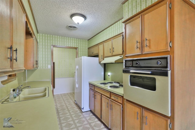 kitchen with a textured ceiling, white appliances, and sink