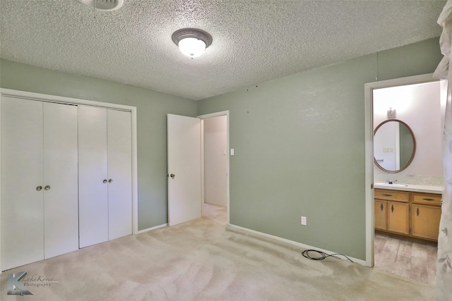 unfurnished bedroom featuring ensuite bathroom, light colored carpet, a textured ceiling, and a closet