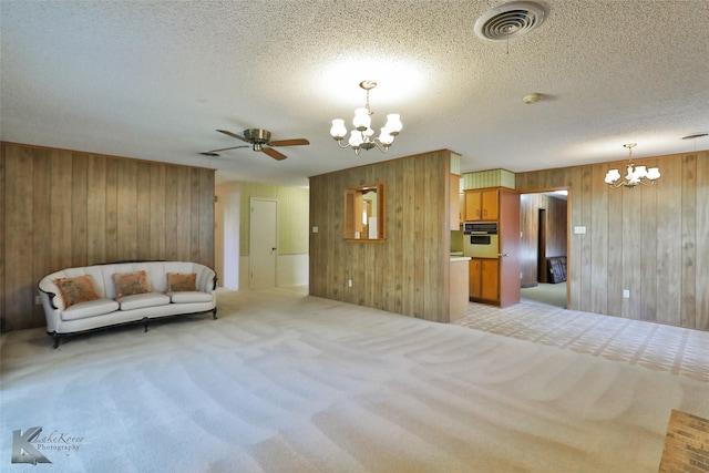 unfurnished living room featuring a textured ceiling, wooden walls, light colored carpet, and ceiling fan with notable chandelier