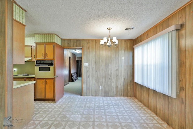 kitchen with a textured ceiling, a chandelier, black oven, hanging light fixtures, and wood walls