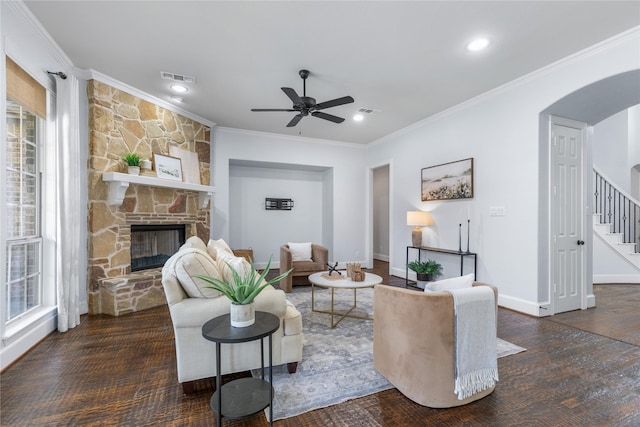 living room featuring a stone fireplace, dark wood-type flooring, ornamental molding, and ceiling fan