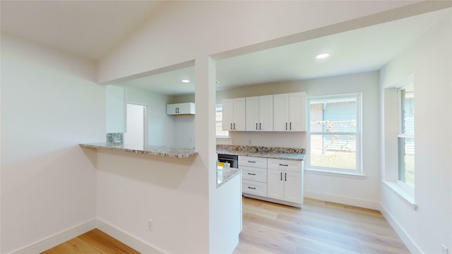 kitchen featuring white cabinets, vaulted ceiling, light stone countertops, and light hardwood / wood-style floors