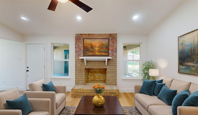 living room with light hardwood / wood-style floors, ceiling fan, and a brick fireplace