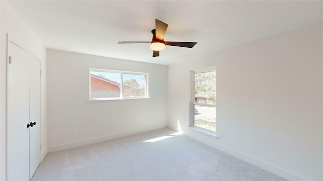 empty room with ceiling fan, light colored carpet, and a wealth of natural light